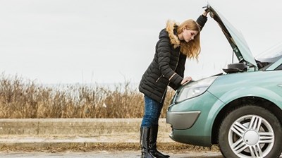 A woman has broken down and is checking inside the bonnet of her car