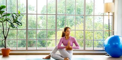 Woman sits in yoga pose in front of large glass windows