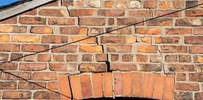 Deep stepped cracks in red brick wall of house