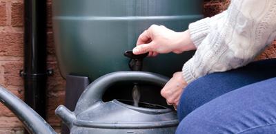 Woman uses water butt to fill watering can 